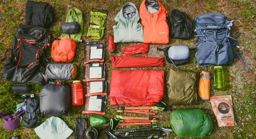 A comprehensive fastpacking gear list, including backpacks, sleeping bags, tents, jackets, food, and trekking poles, laid out on grass.