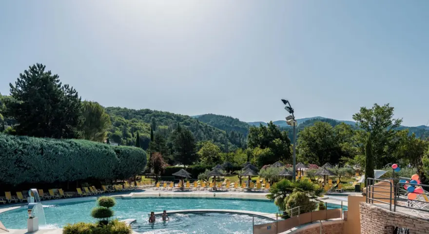 Enjoying a refreshing dip in the pool during a camping trip in Provence. Lush green hills and trees surround the sparkling water, with sun loungers and umbrellas ready for relaxation.