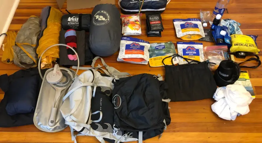 Gear laid out for beginner backpacking: tent, sleeping bag, backpack, water filter, food, and a medical kit.