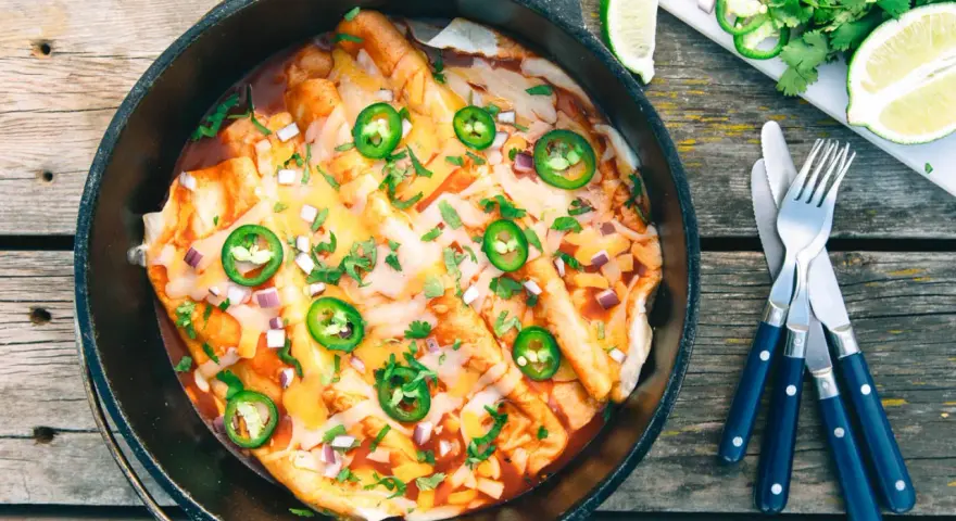 Delicious dutch oven enchiladas, topped with melted cheese, jalapeños, and cilantro, ready to be served.