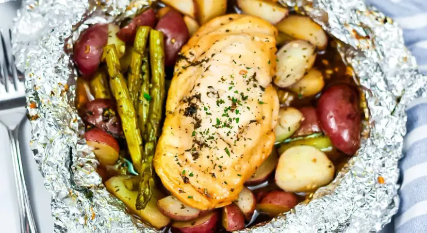 Campfire chicken foil packets in oven, with roasted potatoes and asparagus, seasoned with herbs.