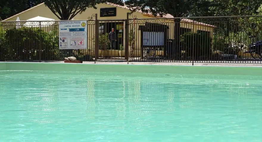 A refreshing pool awaits at this camping in Aix en Provence. A sign details pool depths, and a man stands near the reception building.