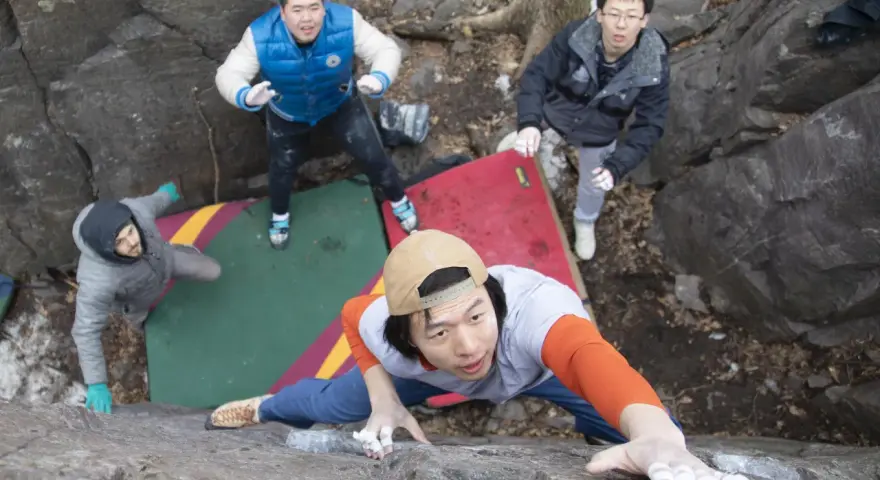 Four friends enjoy bouldering, a type of rock climbing, on a rocky outdoor course with crash pads.