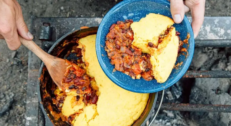 Serving hearty chili and cornbread from a Dutch oven over a campfire. This is easy camp food at its finest.