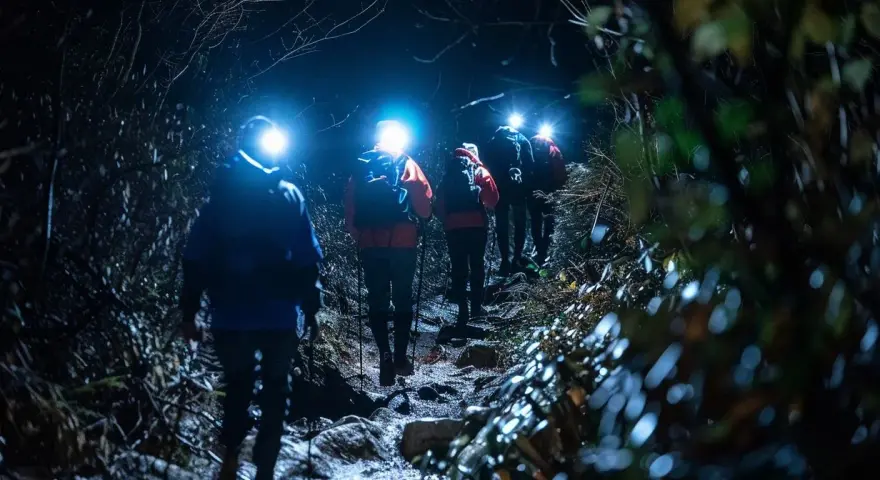 Hikers with headlamps navigate a dark, rocky trail, illuminated by their lights. These are some of the best night hiking tips.