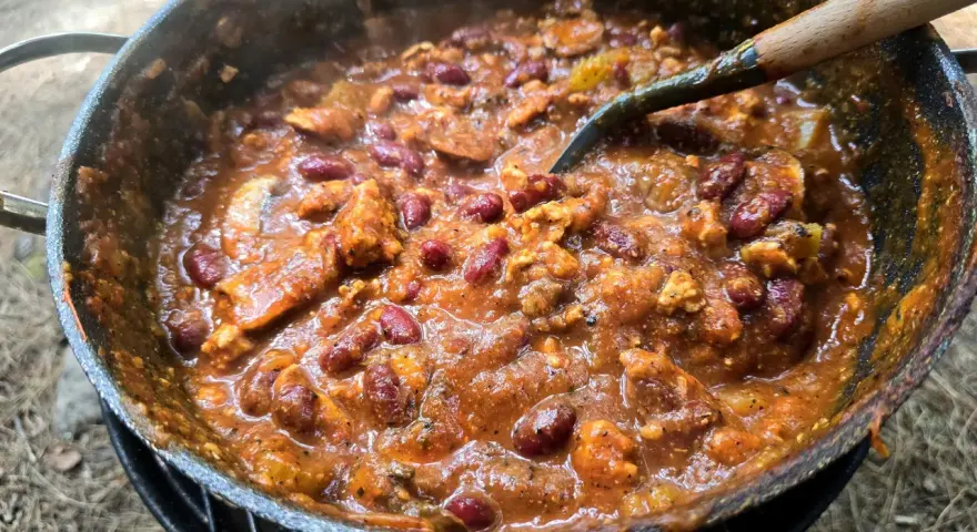 A hearty dutch oven chilli, bubbling and steaming, with kidney beans and chunks of meat, ready to be served.