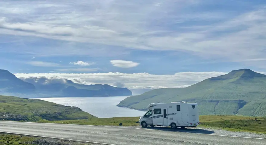 A white RV parked on a scenic road overlooking a bay and green mountains. This view is perfect for the best RV trip planner.