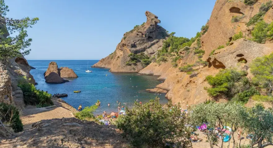 A vibrant scene of camping calanques, with people enjoying the turquoise waters and rocky shores under a clear blue sky.