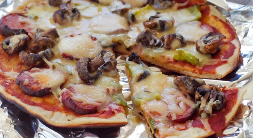 Delicious grilled pizza ideas: a pizza with mushrooms, sausage, and melted cheese on foil.