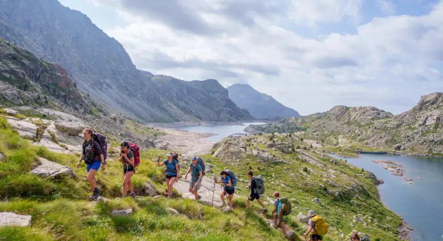 Hikers trek through a scenic mountain landscape, enjoying hiking the Pyrenees Spain. A chain of lakes and rugged peaks stretch into the distance under a cloudy sky.