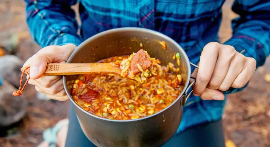 A wooden spoon scoops a hearty portion of campfire jambalaya from a pot.