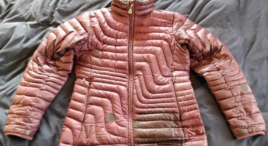 A maroon puffer jacket lies on a dark, wrinkled surface, ready for cleaning. Learn how to wash a down jacket to keep it fluffy and warm.
