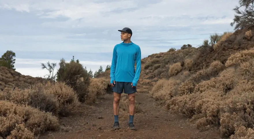 Runner in blue shirt and shorts on a dusty trail, contemplating the disadvantages of merino wool, like its tendency to hold moisture in humid conditions.