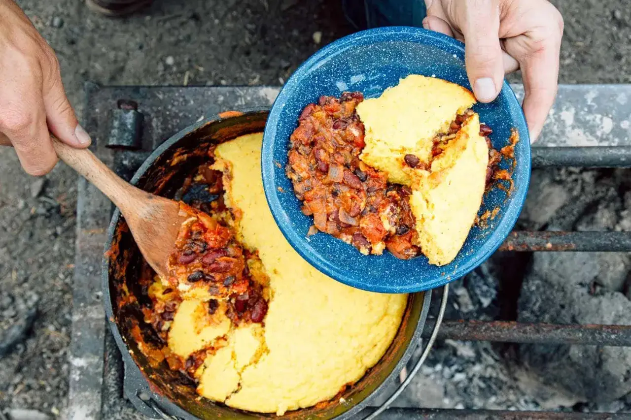 Serving hearty chili and cornbread from a Dutch oven, a perfect example of delicious camping meals.