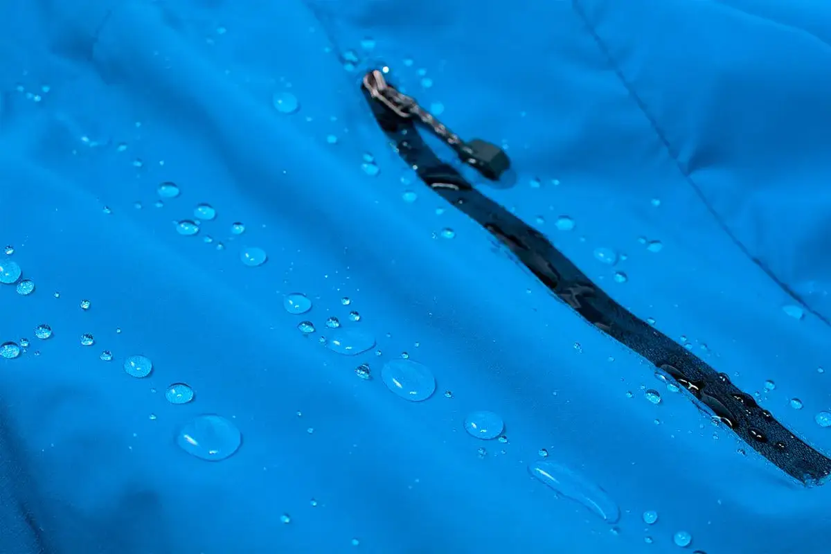 Water beads on a blue jacket, showcasing its effective dwr coating. The fabric repels moisture, keeping you dry.