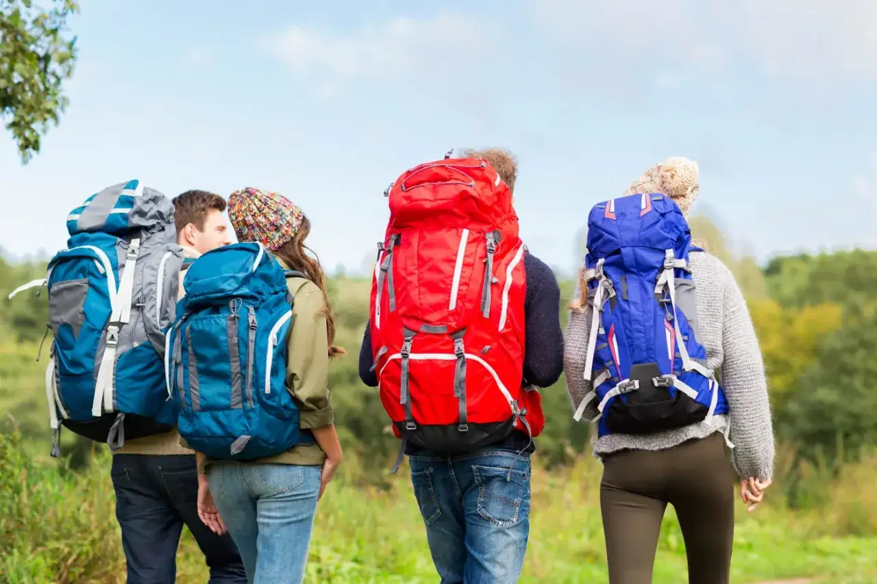 Four friends, each with a large backpack, walk on a trail. The hiking backpack vs travel backpack debate is settled by their gear choices.