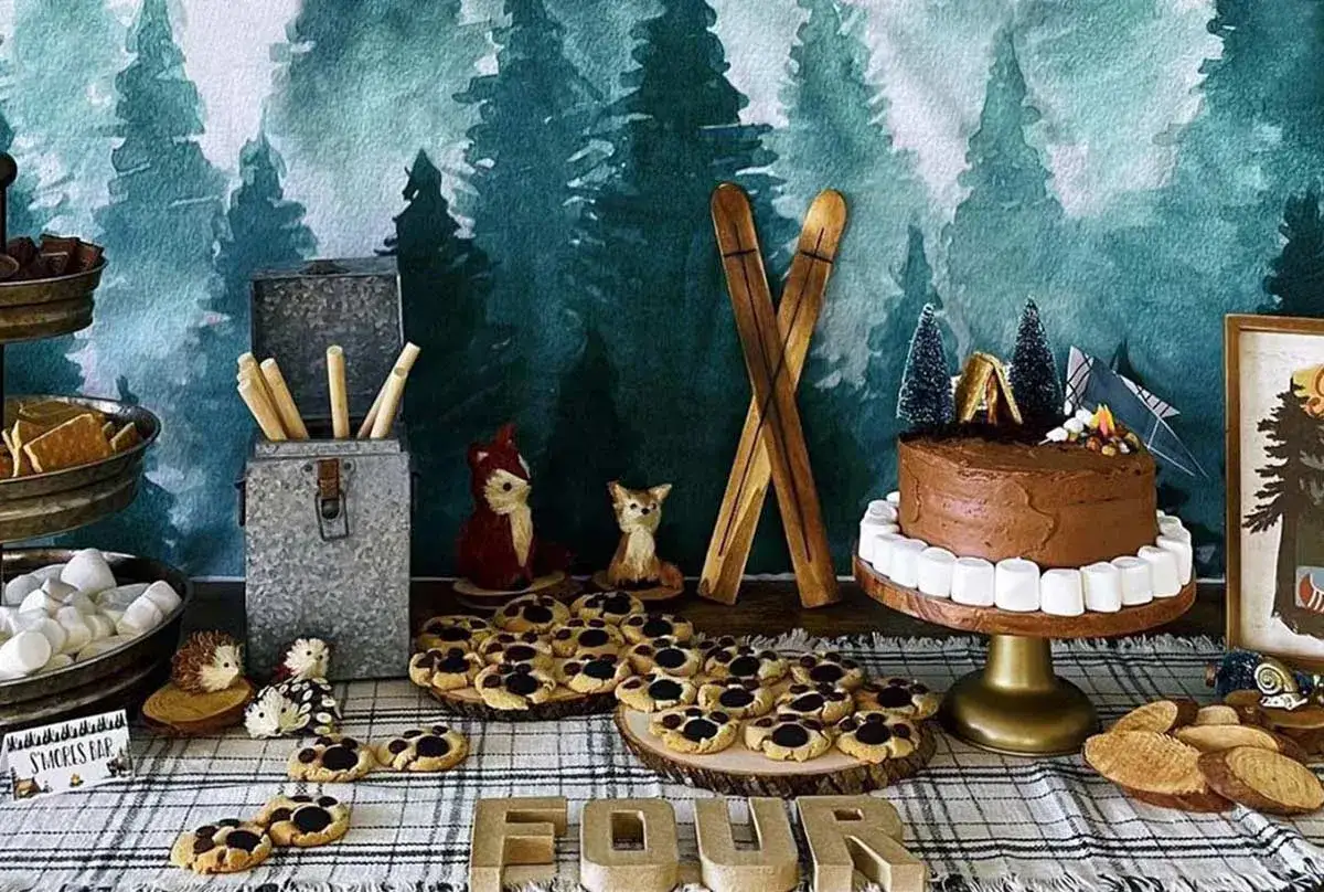 A woodland-themed dessert table with a chocolate cake, cookies, and s'mores supplies, perfect for camping party ideas.