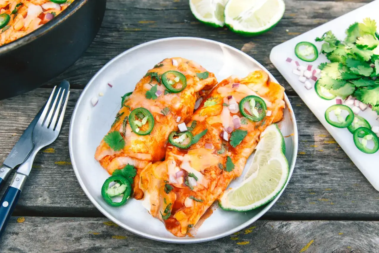 Delicious dutch oven enchiladas, topped with jalape&ntilde;os, cilantro, and red onion, served with lime wedges.