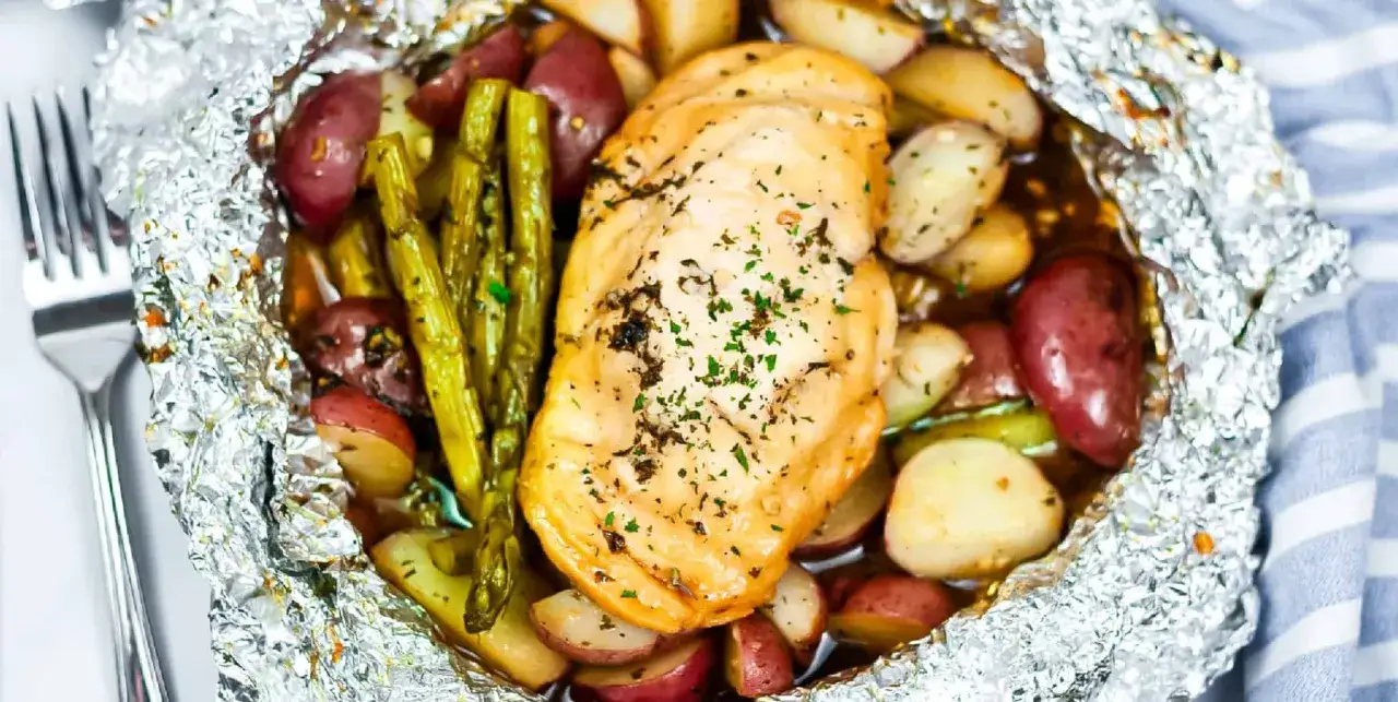 Juicy chicken breast with roasted potatoes and asparagus, all cooked in foil packets, perfect for a campfire meal.