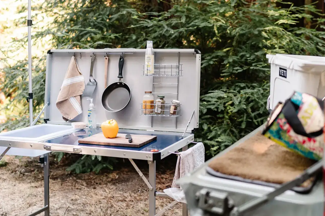 A complete camping kitchen setup with a sink, cutting board, spices, and cooking utensils, ready for outdoor culinary adventures.