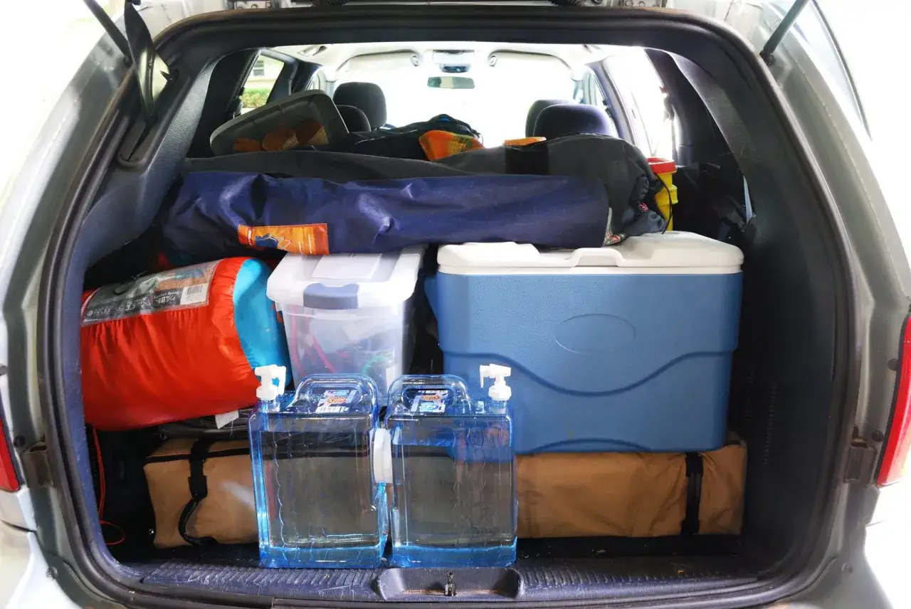 Car camping packing list: sleeping bag, cooler, water jugs, and storage bins are loaded into the back of a car, ready for an adventure.