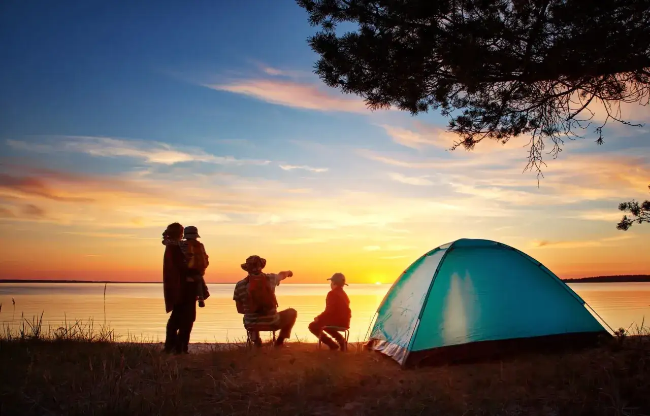 Family enjoys a sunset by the lake, with a tent set up. This scene is perfect for a camping trip checklist, reminding you to pack for beautiful evenings.