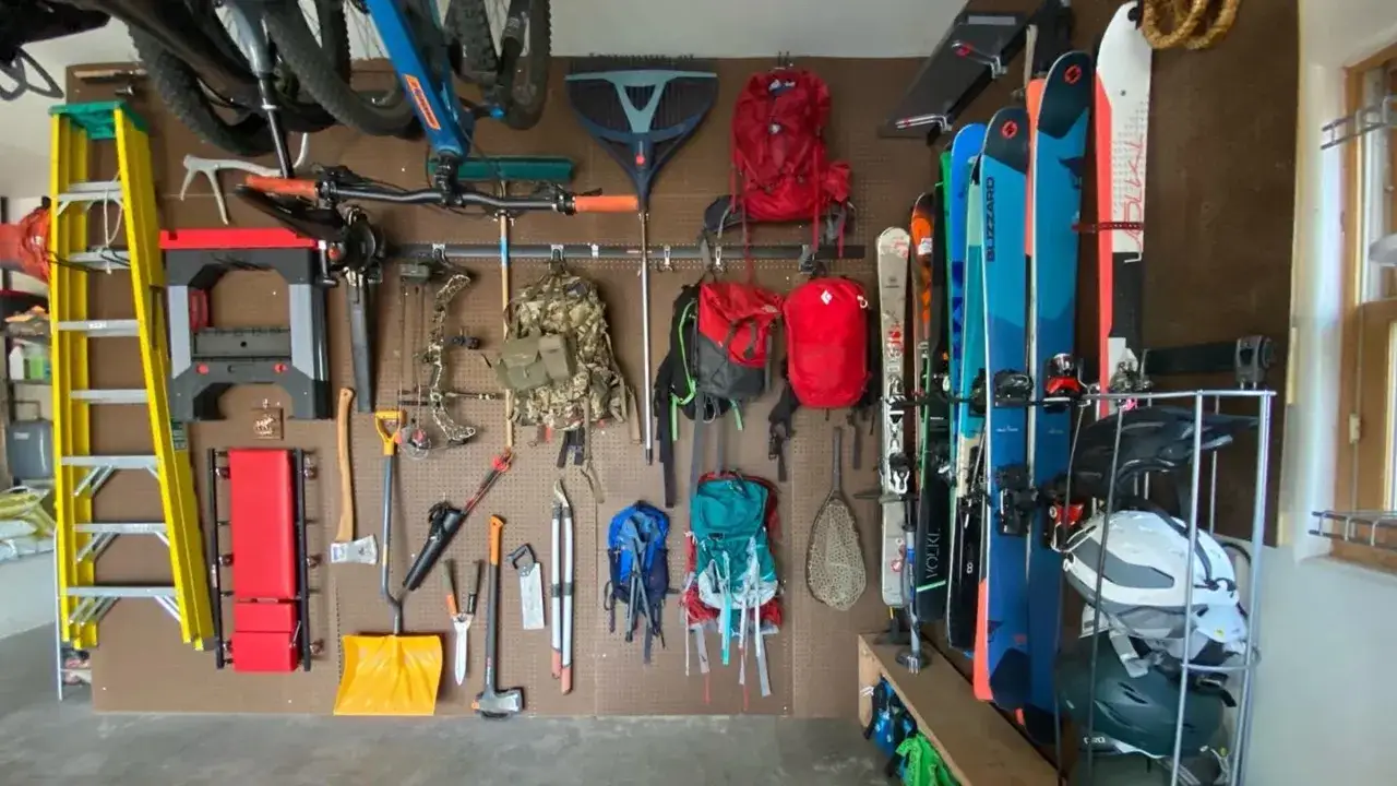 A well-organized garage with pegboard wall storage for camping, skiing, and yard gear. Includes bikes, skis, backpacks, tools, and helmets.