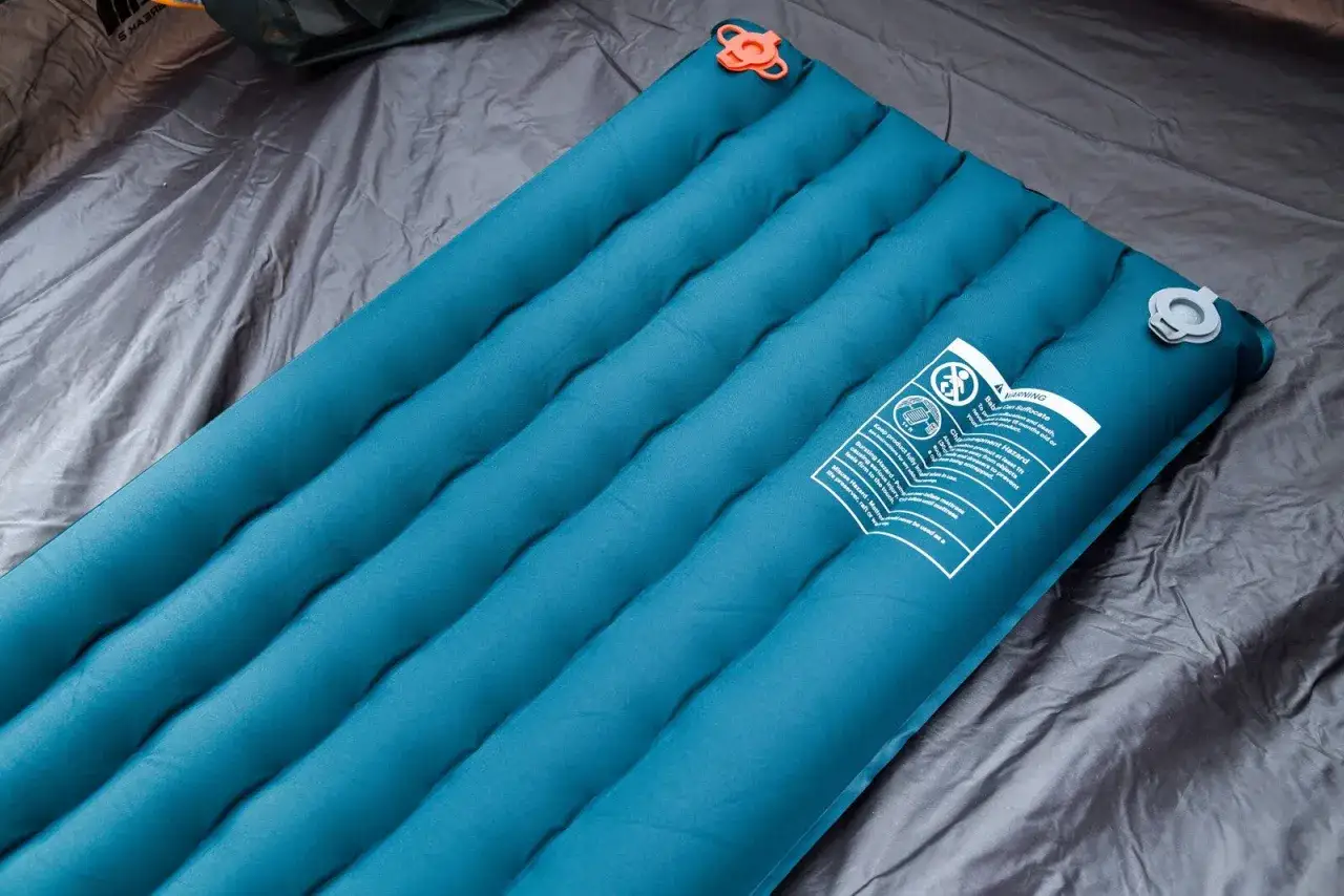 A teal, quilted sleeping pad lies on a gray tent floor. This quietest sleeping pad promises a peaceful night's rest.