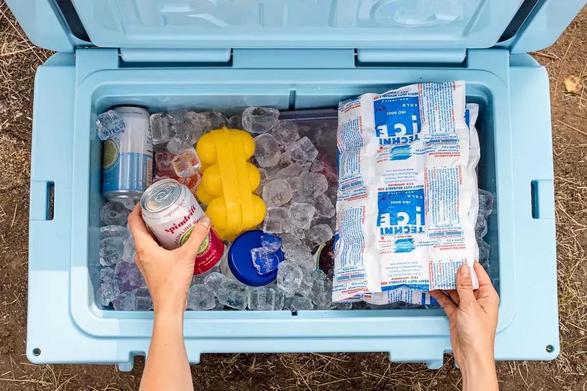 Hands packing a cooler with ice, cans, and reusable ice packs. Learn how to pack a cooler for your next adventure!