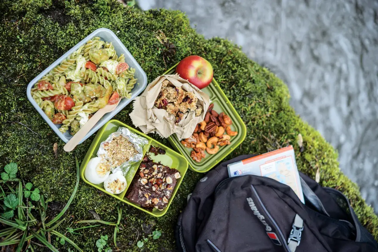 Delicious hiking lunch ideas: pasta salad, brownie, eggs, nuts, granola bar, and an apple, all packed for an outdoor adventure.