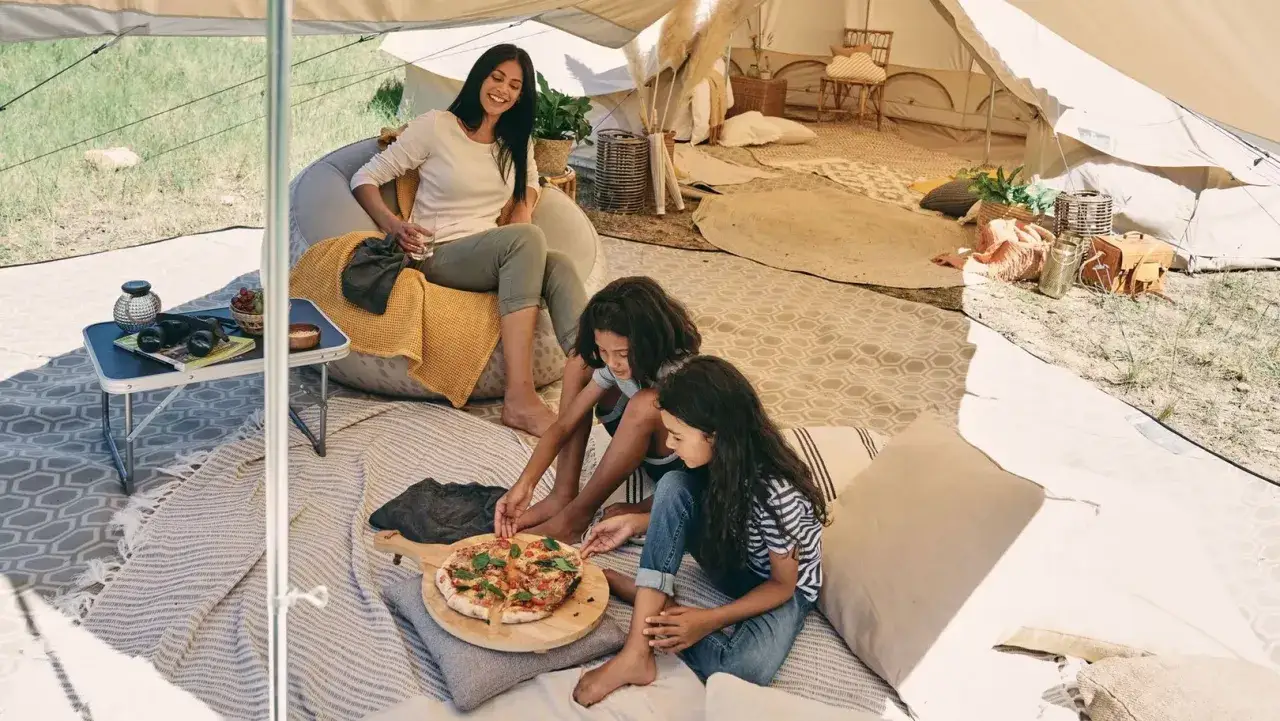 A family enjoys pizza and grapes during camping activities inside a spacious tent.