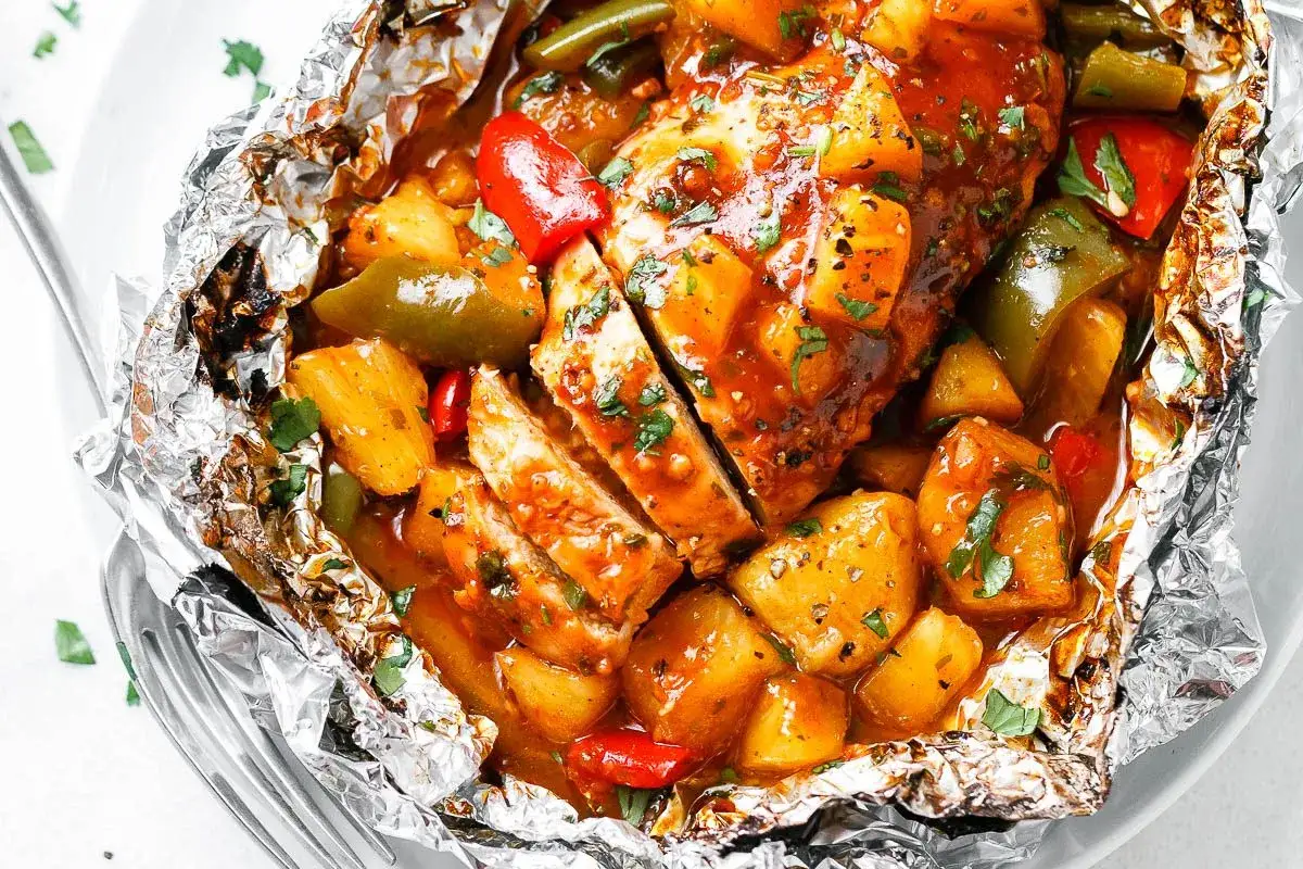 Juicy campfire chicken foil packets in oven, with pineapple, bell peppers, and green beans, all coated in a savory sauce and sprinkled with fresh parsley.
