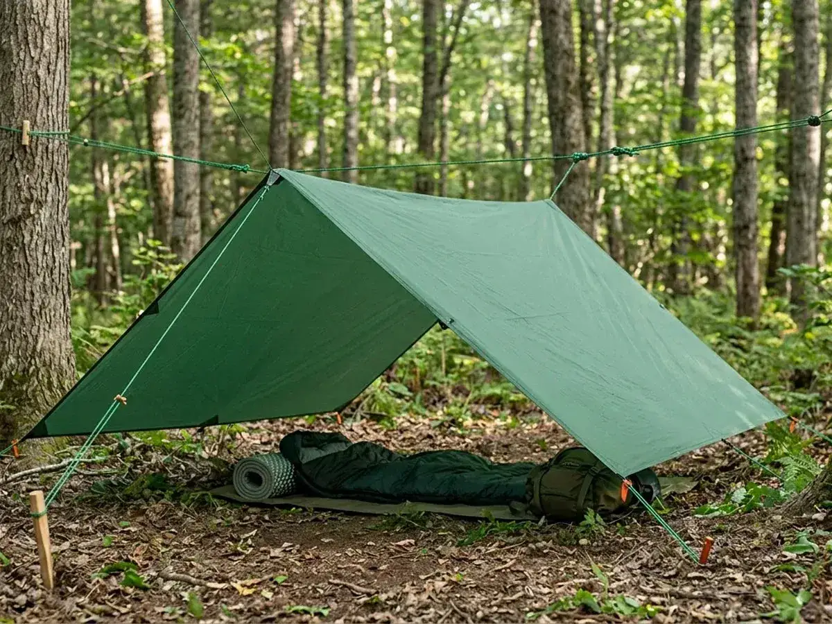 A simple tarp shelter setup in a forest, showcasing effective camping hacks for a minimalist outdoor experience. Sleeping bag and mat are ready.