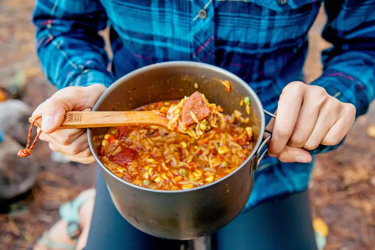 A wooden spoon scoops a hearty portion of campfire jambalaya from a pot.