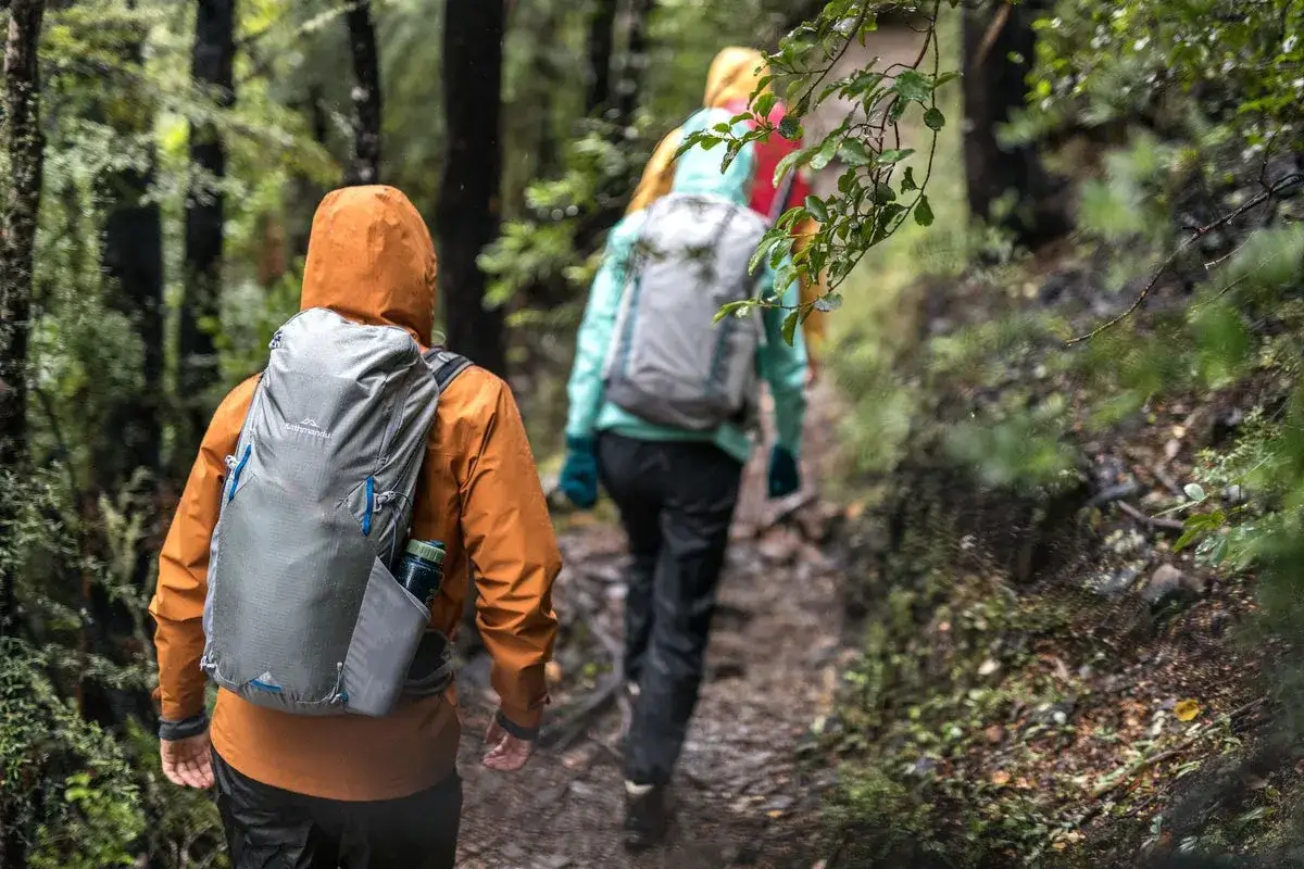 Hikers in a lush forest, with rain falling. One person wears an orange jacket and carries a water bottle.
