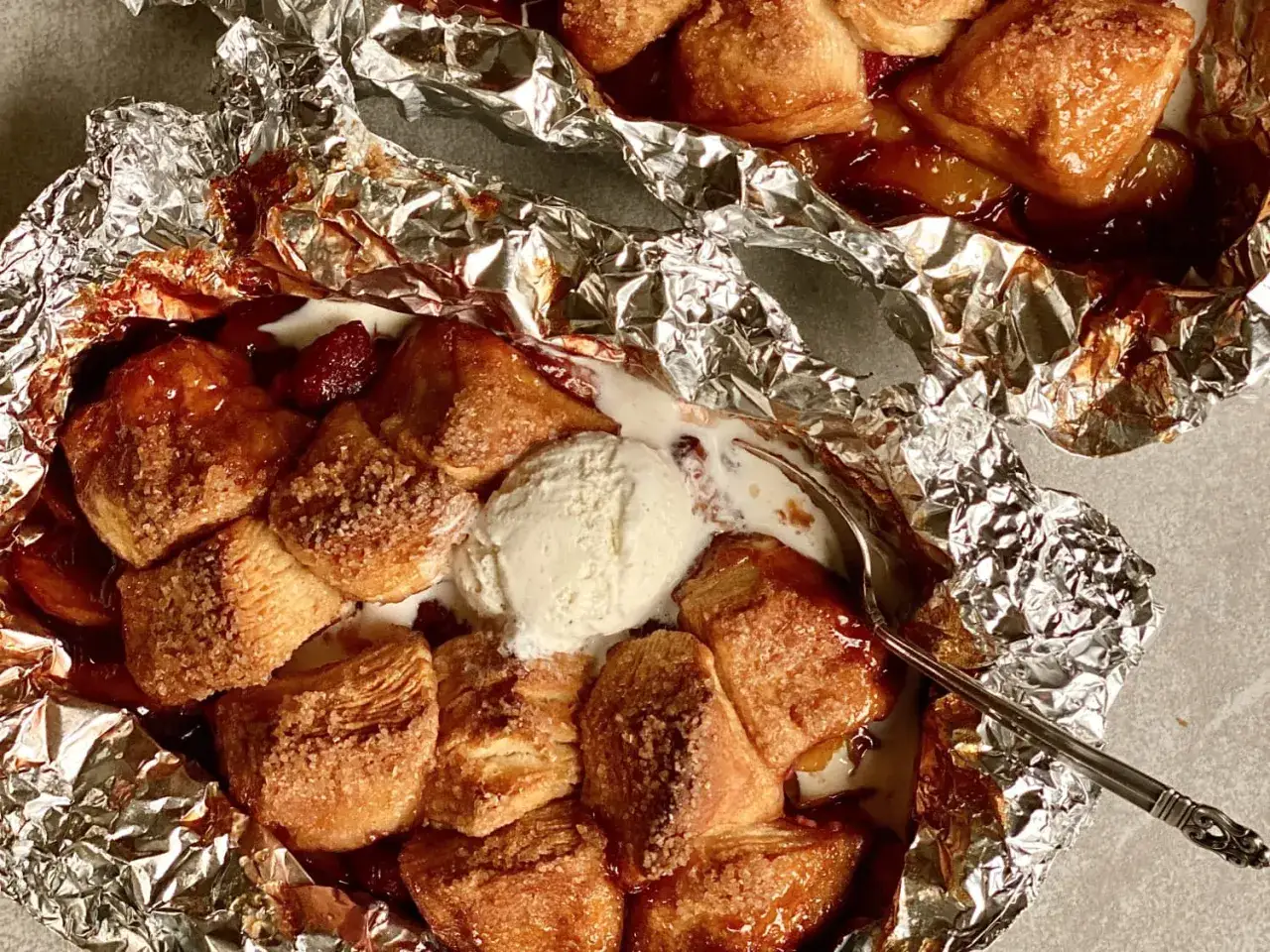 Warm campfire peaches baked in foil, topped with a scoop of melting vanilla ice cream and a sprinkle of cinnamon sugar.
