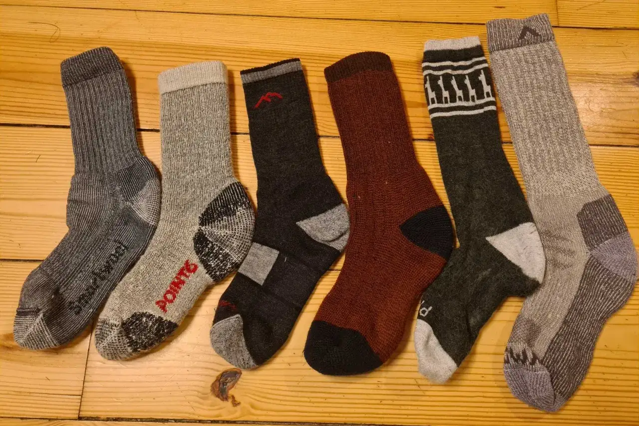 A collection of what are hiking socks, in various colors and patterns, laid out on a wooden surface.