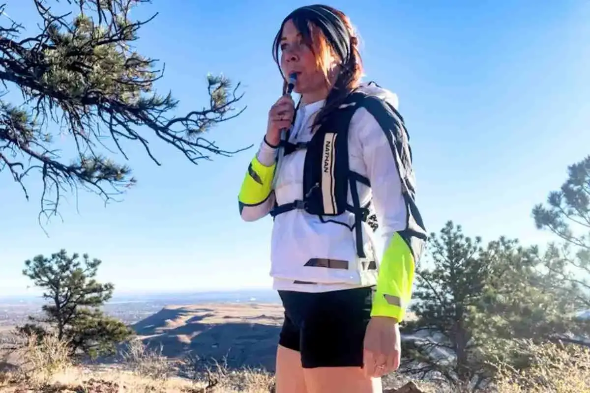 A runner drinks from a hydration pack on a mountain trail.