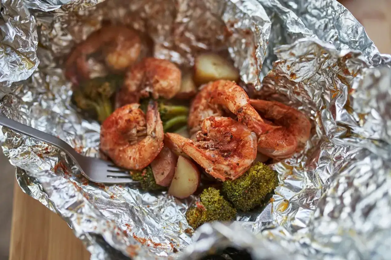 Shrimp and potato foil packets in oven, with broccoli and a fork.