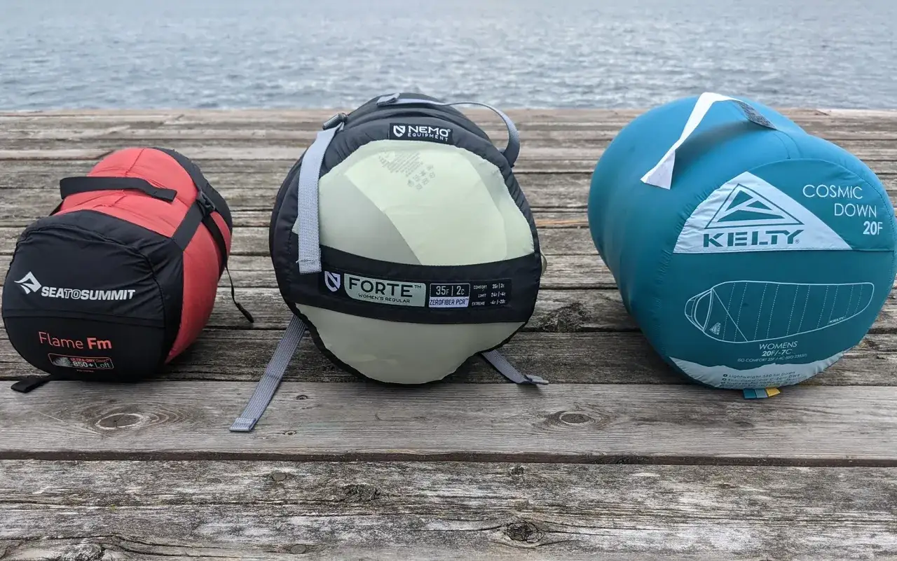 Three sleeping bags on a dock: a red Sea to Summit down bag, a Nemo synthetic bag, and a teal Kelty down bag.