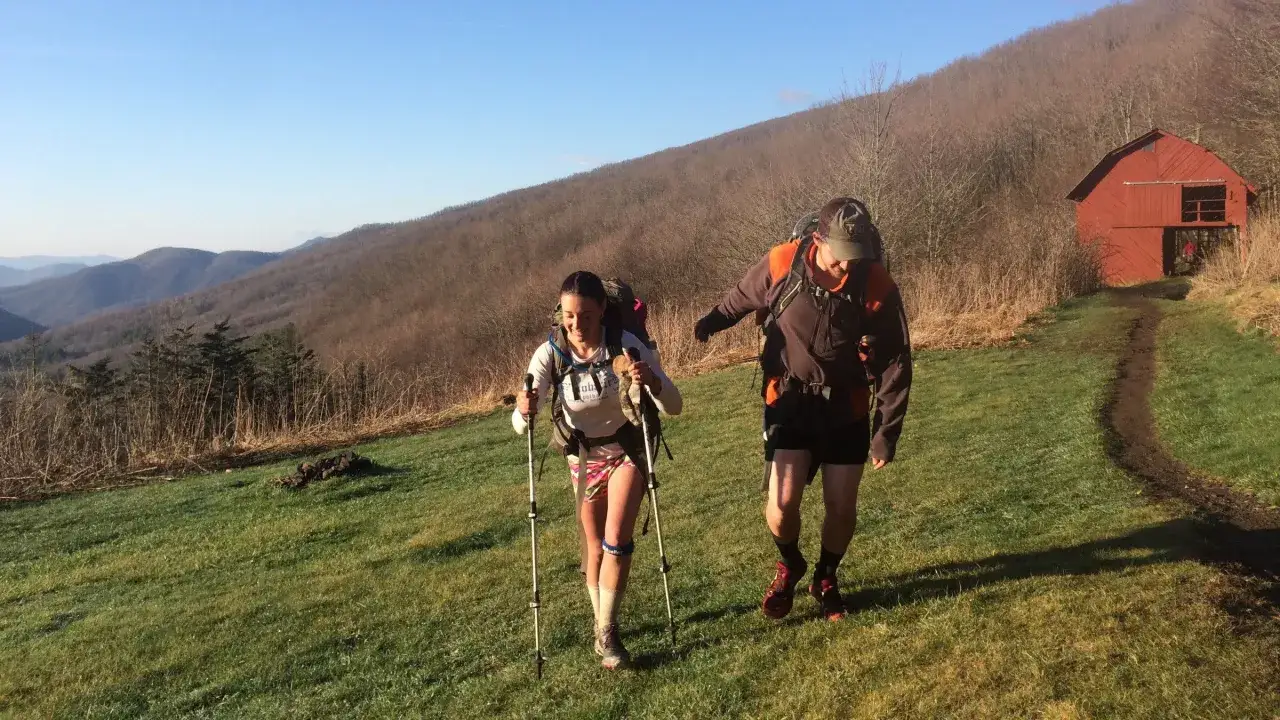 Two people trekking up a grassy hill towards a red barn. This scene captures the essence of trekking, a more immersive journey than a simple hike.