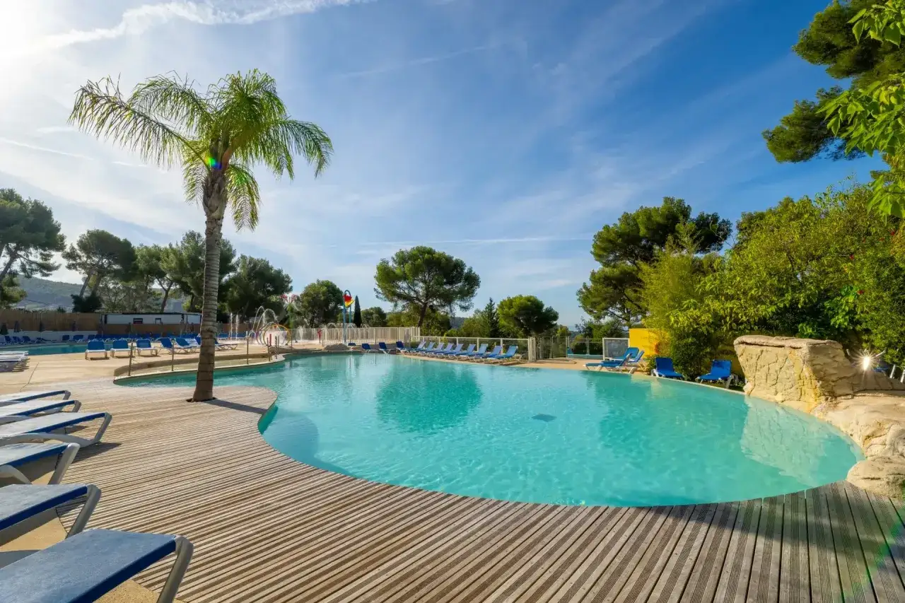 Sunny day at a resort with a large pool, palm trees, and lounge chairs. Imagine staying in a mobil home near Cassis and enjoying this view.
