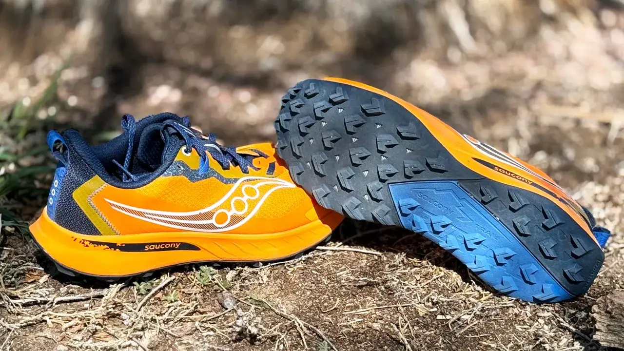 Orange and blue Saucony trail running shoes sit on the ground, ready for adventure.