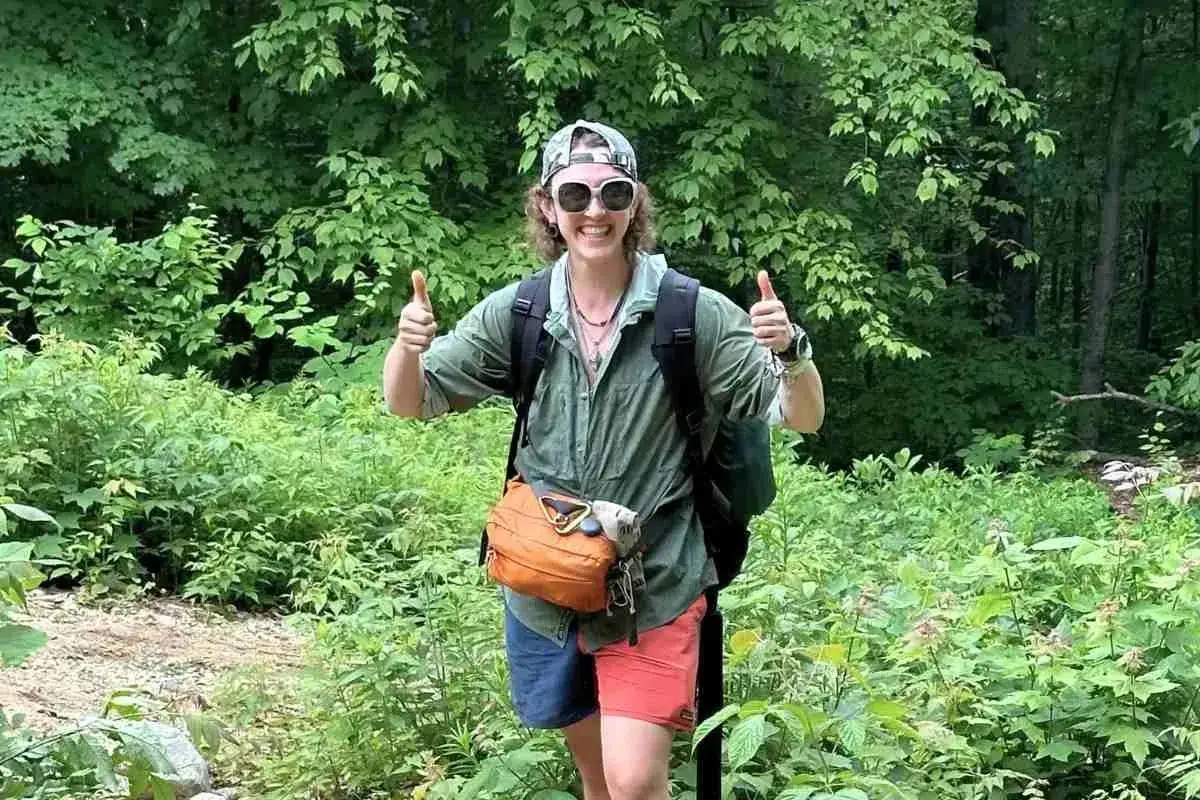 A hiker in a green, breathable hiking shirt material, gives a double thumbs-up. He's ready for adventure!