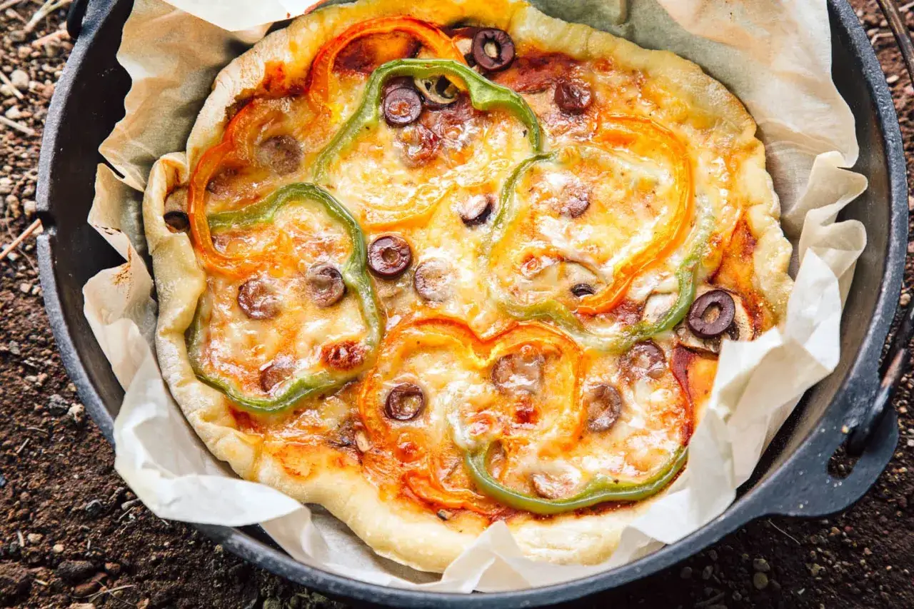 A delicious dutch oven pizza camping meal, topped with colorful bell peppers and olives, baked to cheesy perfection.