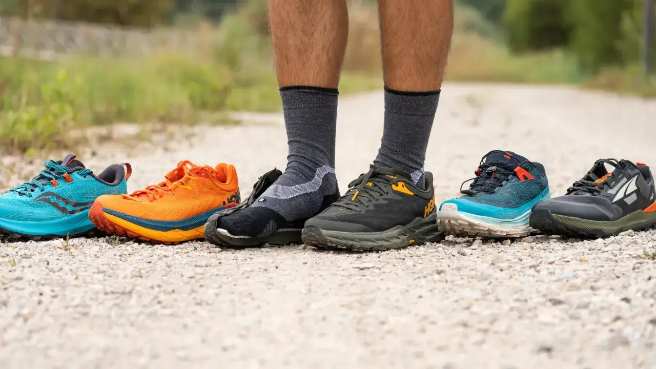 A person stands on a gravel path, showcasing a variety of trail running shoes vs hiking shoes in vibrant colors.