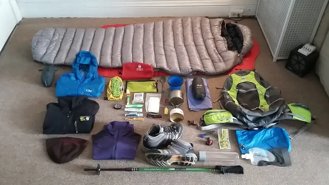 Gear for hiking and backpacking: sleeping bag, backpack, jackets, shoes, water bottles, and camping essentials laid out on the floor.