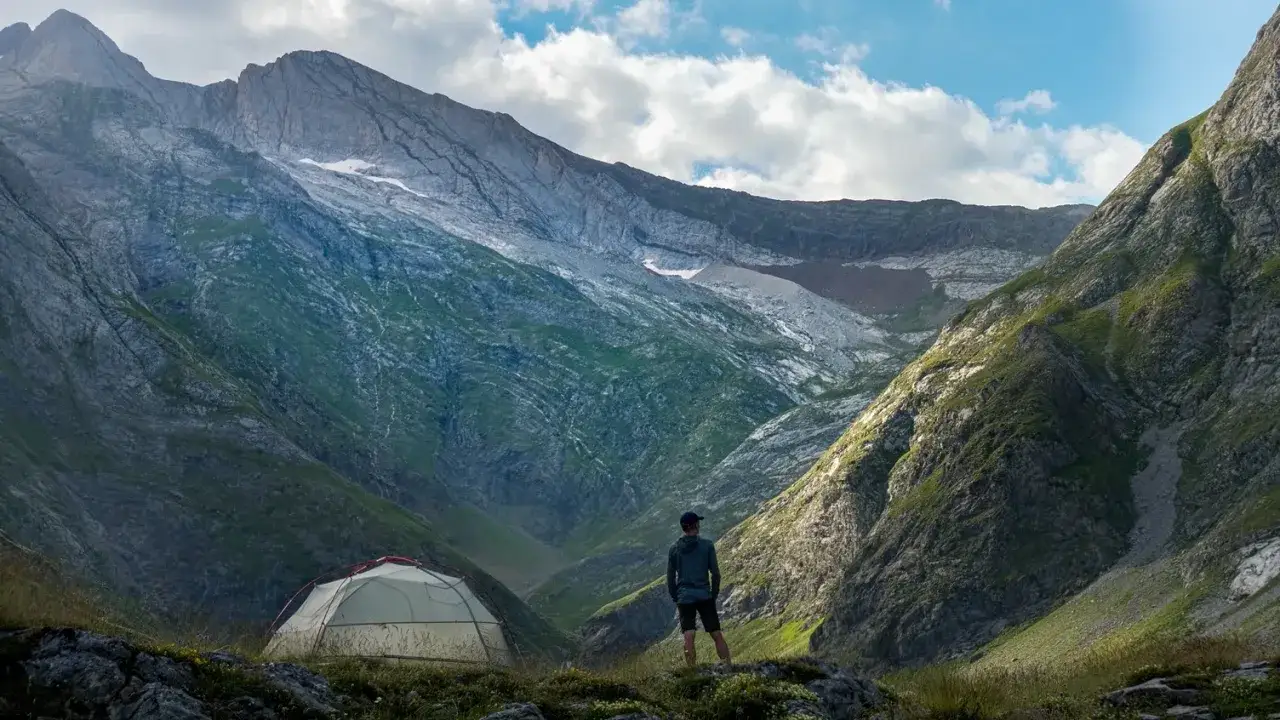 A lone hiker stands amidst a breathtaking valley, a tent pitched nearby, ready for an adventure in the Pyrenees, France.