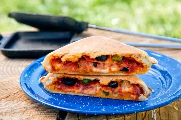 A delicious pie iron pizza, cut in half and stacked, reveals melted cheese, pepperoni, olives, and peppers.