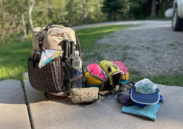 Ready for adventure! A large backpack, hiking poles, water bottle, and colorful pouches are laid out with camping gear, including a hat and gloves.